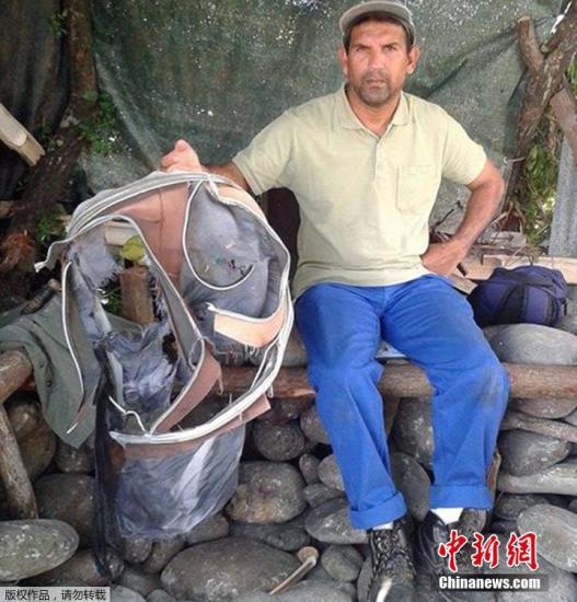 圖為當?shù)貢r間7月30日，留尼旺島上的一名海岸清潔人員展示他找到的一個手提箱的殘骸。